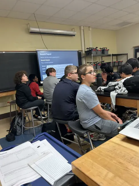 Students watching a research proposal presentation in class